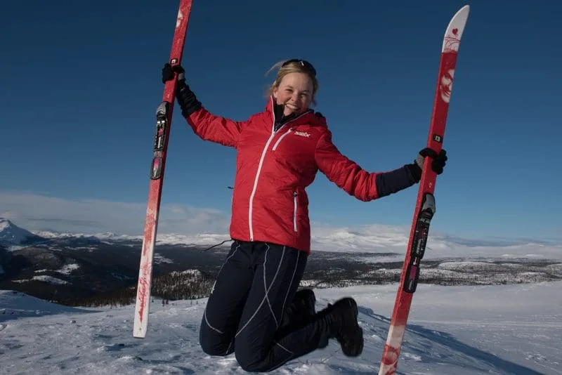 Smiling woman jumps and holds skis