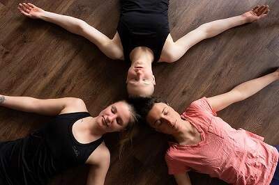 Three people practise yoga lying in savansana