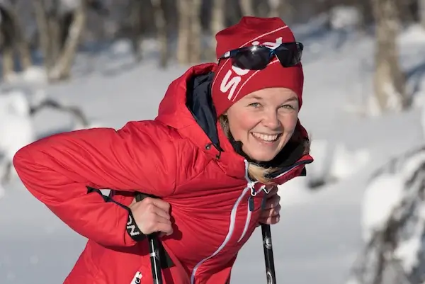 Female cross country skier, wearing red, smiles at the camera